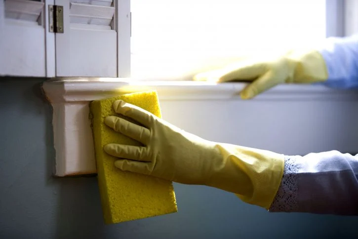 hand with rubber glove holding a sponge while cleaning a window frame