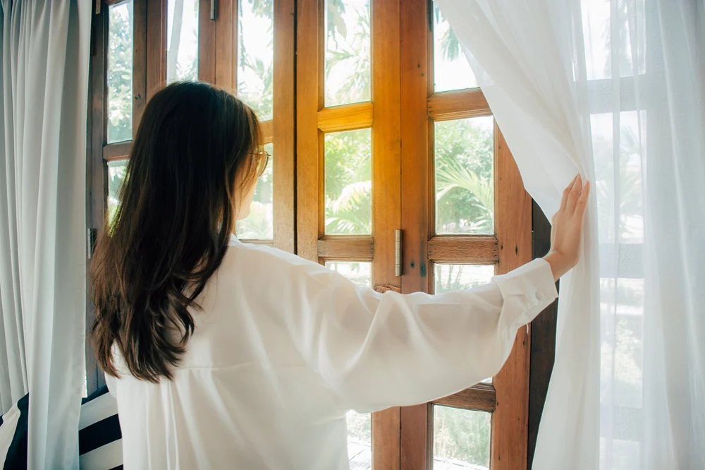 woman holding curtains to the side of large doors