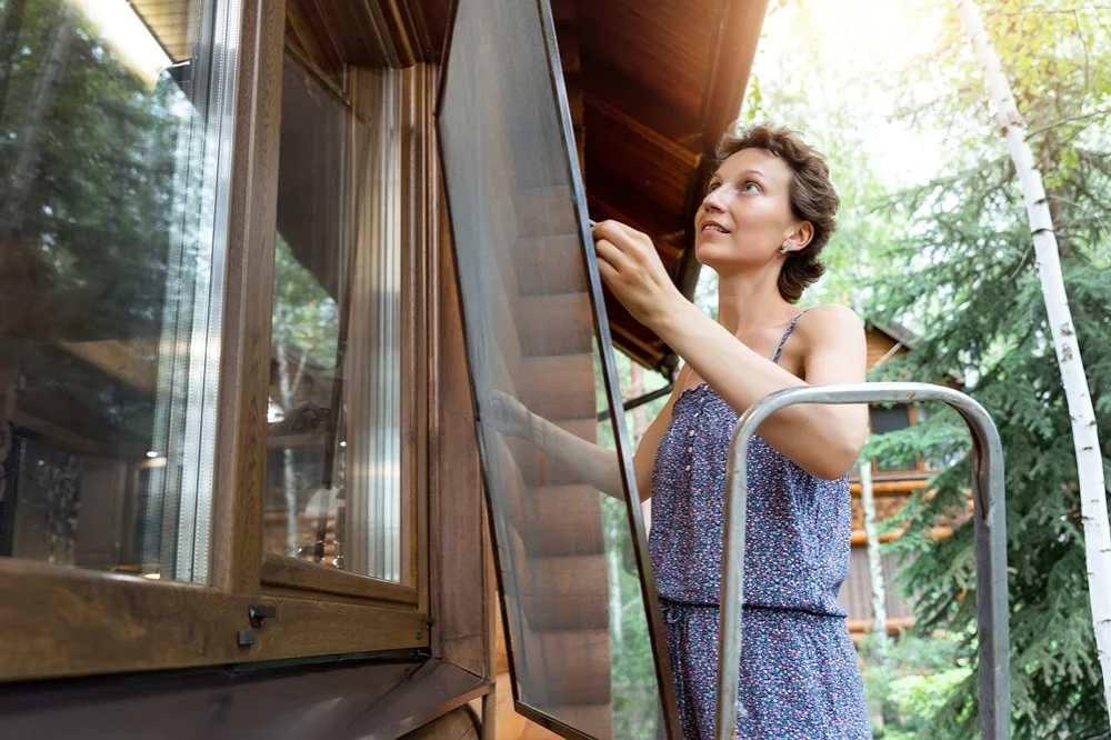 woman reinstalling a window screen while on a small ladder