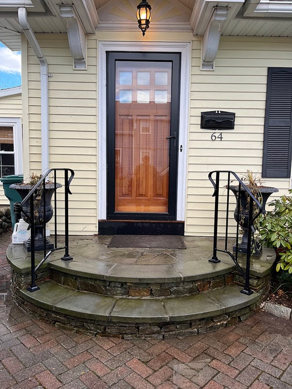 wrought iron stair railing installed on a yellow house with a black storm door