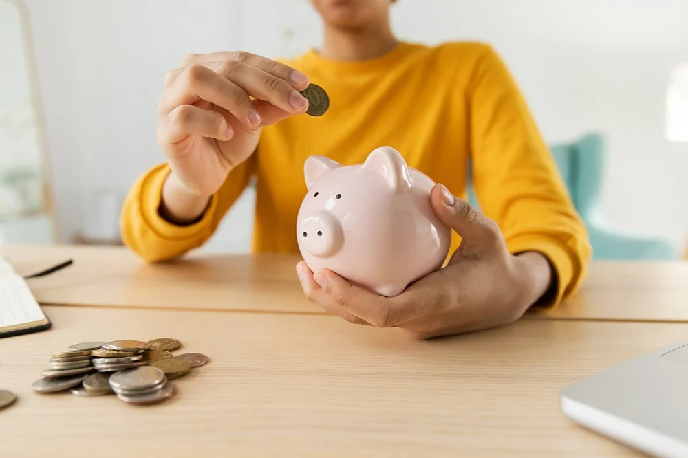 woman in yellow shirt placing coins into a piggy bank