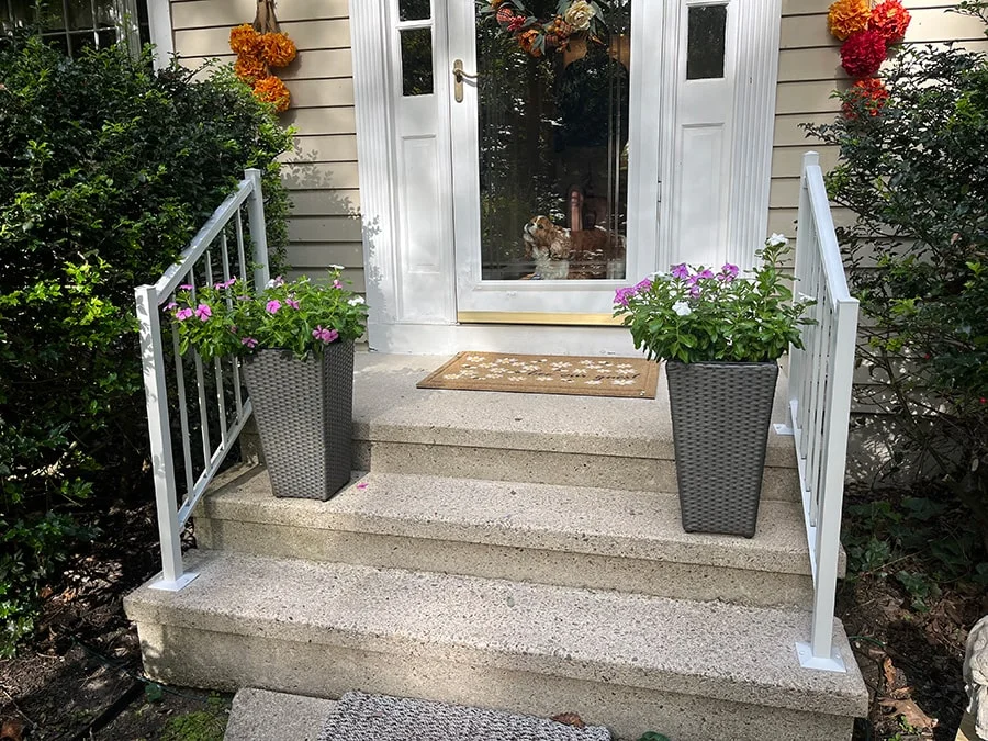 white aluminum railings on a tan house with planters on the stairs