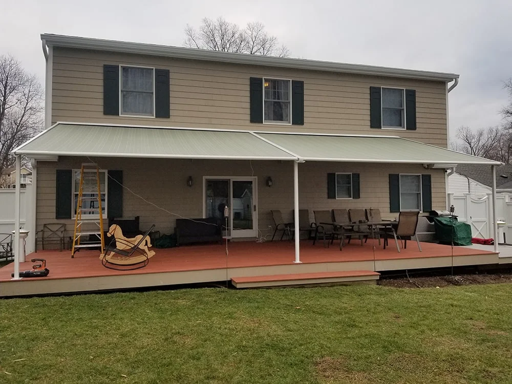 retractable awning with poles on a home with yellow siding and dark shutters