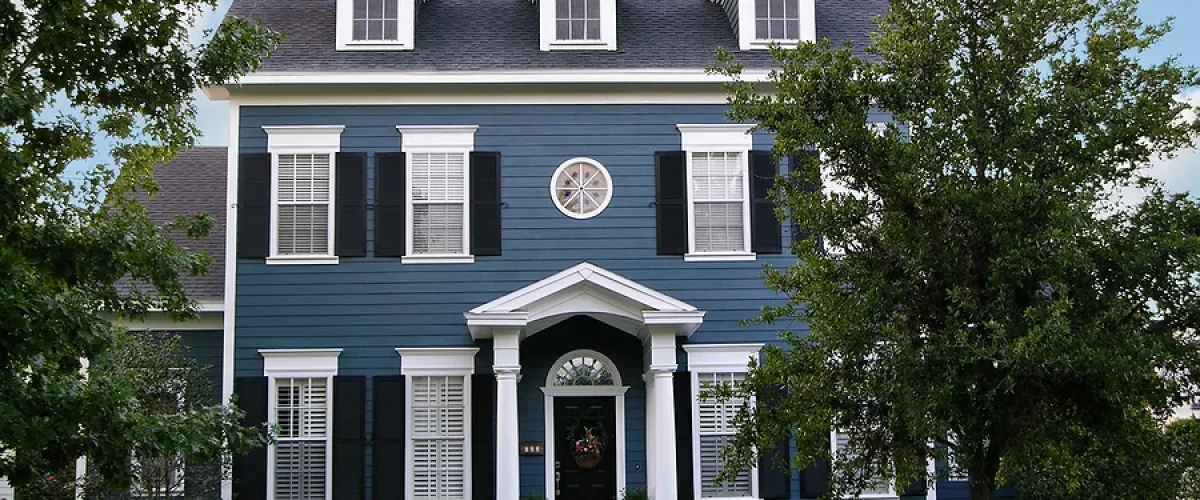 blue three-story colonial style home with black window shutters