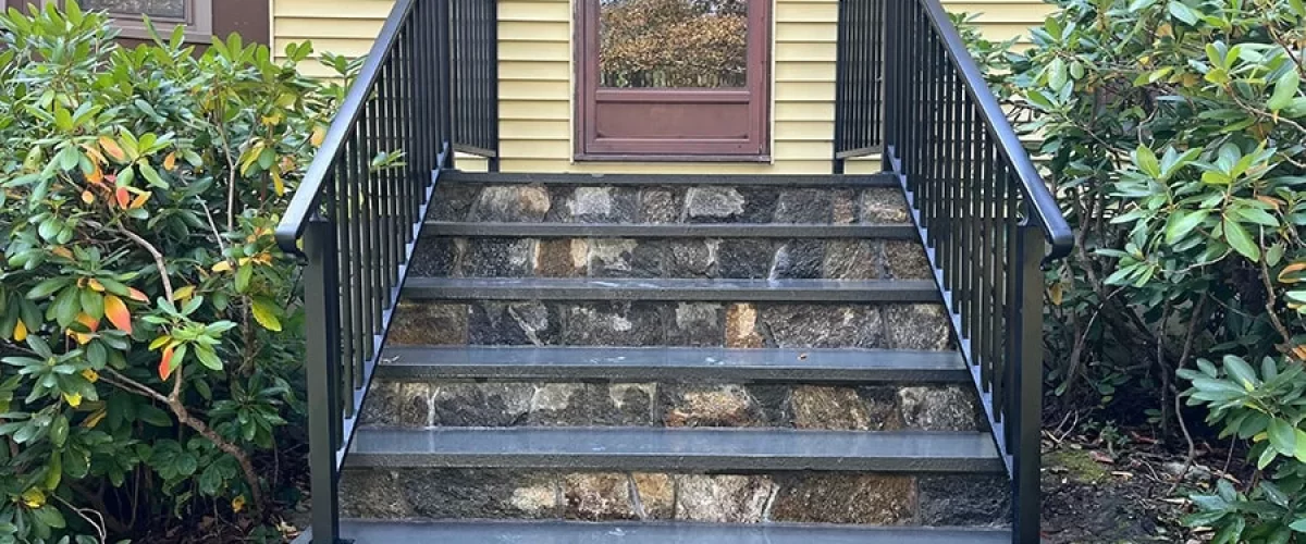 black aluminum porch railing on a yellow house with brown entry door