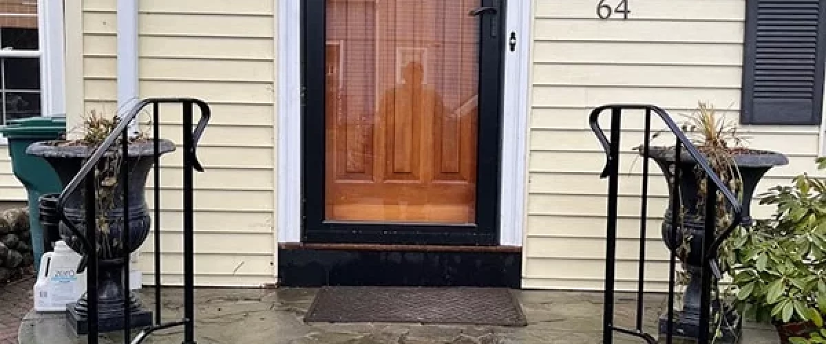 wrought iron stair railing installed on a yellow house with a black storm door