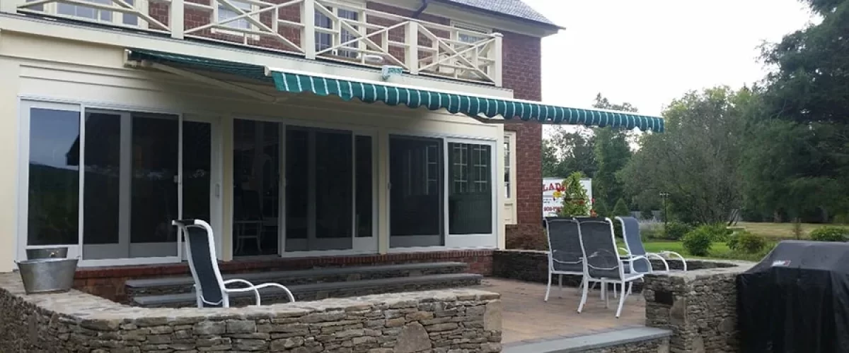 green retractable awning with white stripes covering an outdoor patio