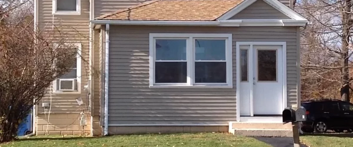 tan vinyl siding, white replacement windows, and gutters installed