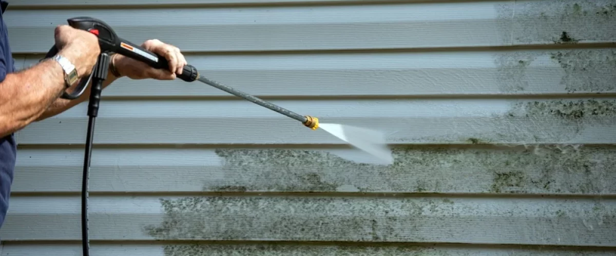 older gentleman power washing dirty vinyl siding