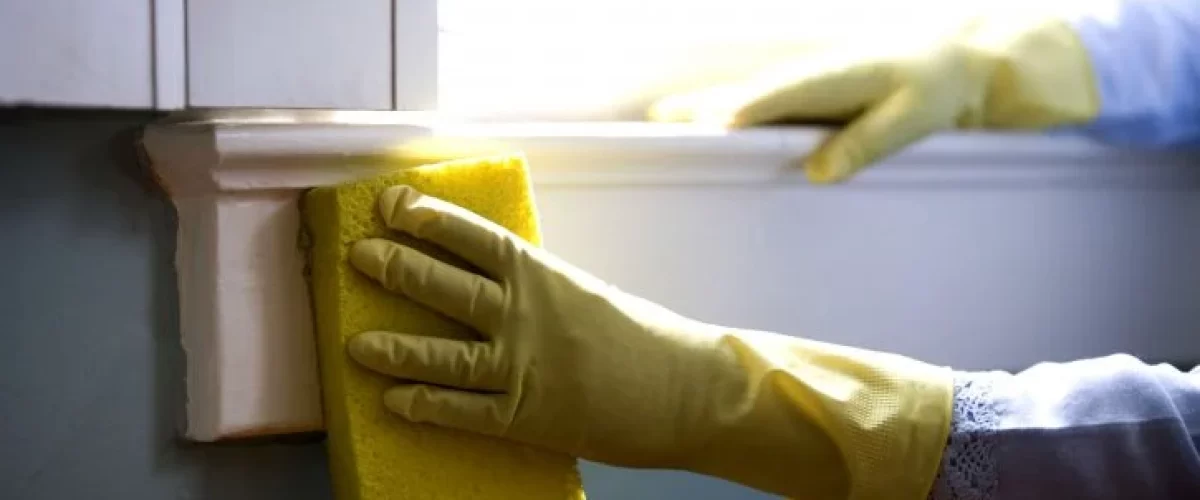 hand with rubber glove holding a sponge while cleaning a window frame