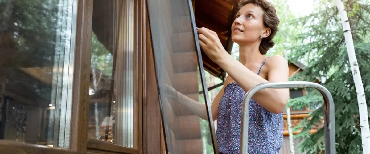 woman reinstalling a window screen while on a small ladder