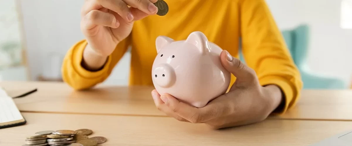 woman in yellow shirt placing coins into a piggy bank